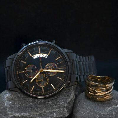 Stylish black wristwatch on stone with a copper ring, perfect for sophisticated fashion.