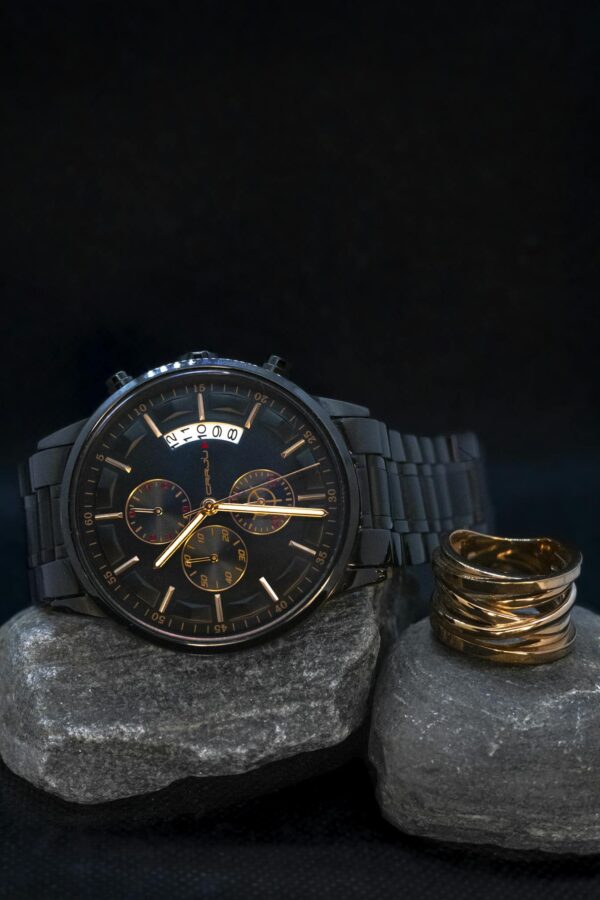Stylish black wristwatch on stone with a copper ring, perfect for sophisticated fashion.